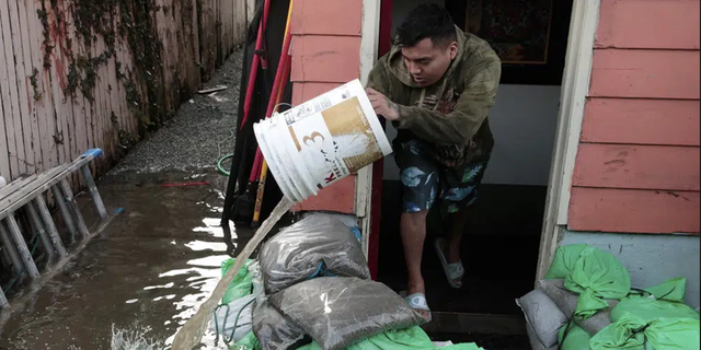 Manuel Israel Archila Lopez uses a bucket to scoop water from his family's home in Seattle's South Park neighborhood on Tuesday morning.